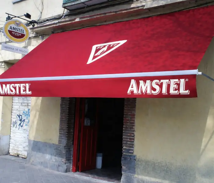 Toldo de lona roja con cenefa blanca sobre la puerta de un bar